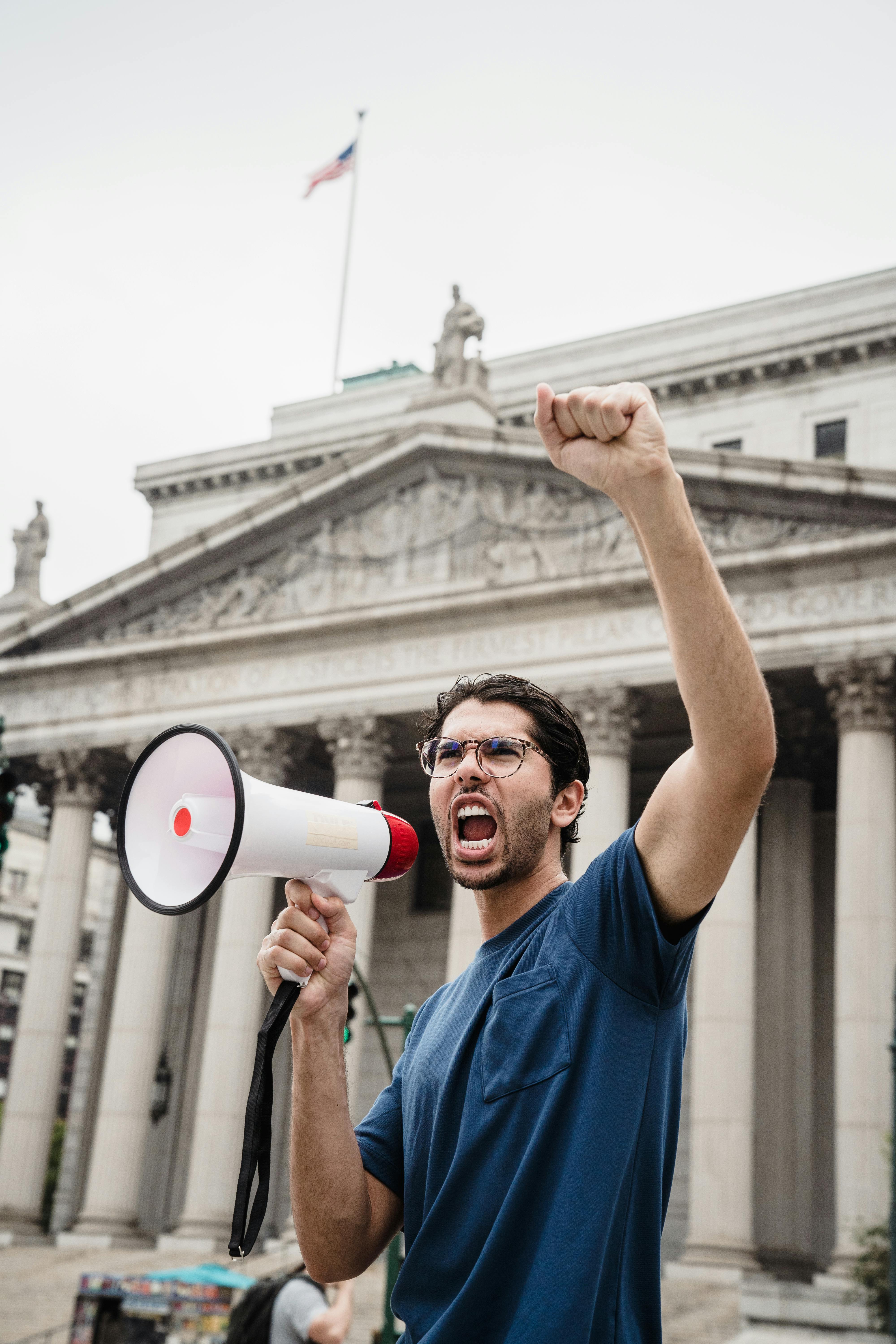 A passionate protester speaks through a megaphone during a rally by a government building.